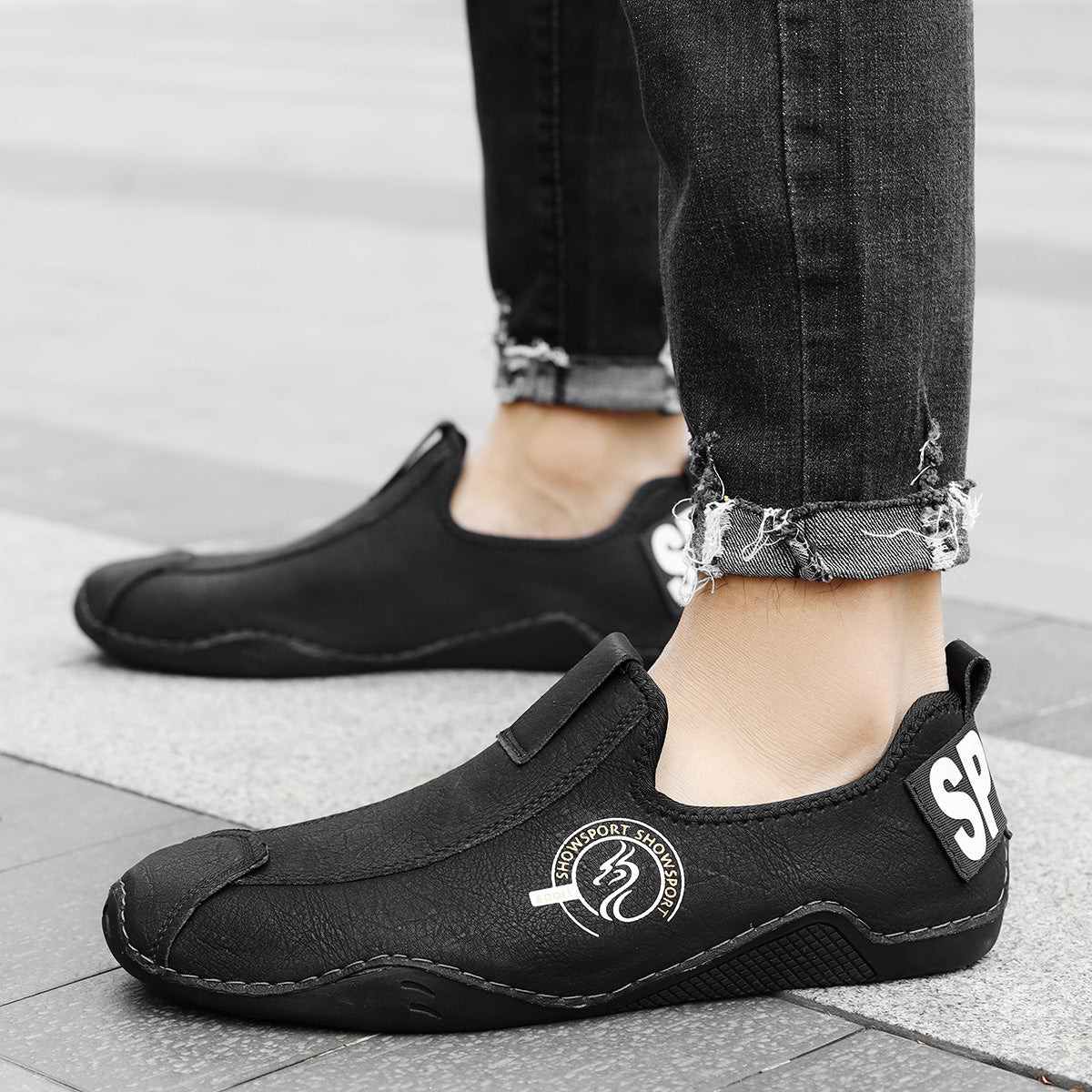 Black shoes worn with rolled-up jeans on a neutral background